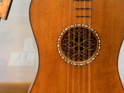 [A view of the hole in the body of the guitar. There is a white color detail (possibly pearl inlay) around the hole. The hole itself has a lace effect wood carving within it.]